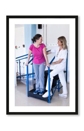 Vertical photo of a physiotherapist stands in the hospital next to her patient as they look at each other and laugh together.