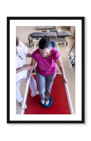 A female physiotherapist and her patient are doing rehabilitation on the parallel bars in the hospital. Vertical photo.