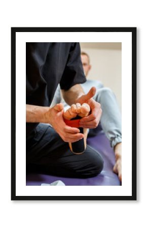 Male physiotherapist doctor massages the feet of a relaxed man sitting on a stretcher. He uses kinesio tape. Taping the foot