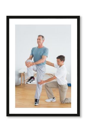 Therapist helping man with stretching exercises in gym hospital