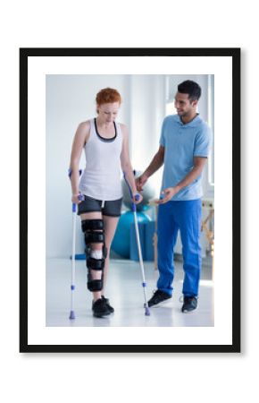 Physiotherapist helping woman with stiffener on the leg walking with crutches