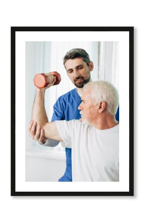 senior man lift a dumbbell, he doing treatment exercise with his physiotherapist. Physio treatment at rehab center