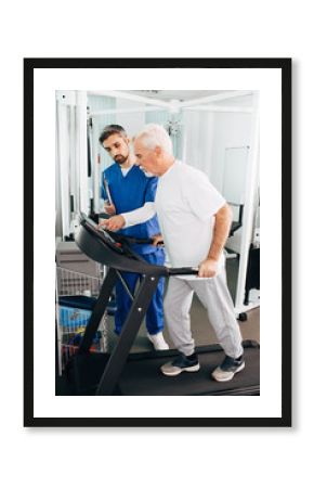 Elderly man is recovering on a treadmill. His physiotherapist helps him recover his body after physical injury.