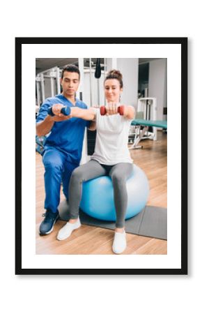 Physiotherapist working with male patient in clinic. Raises dumbbells, strengthening arm muscles and developing joints