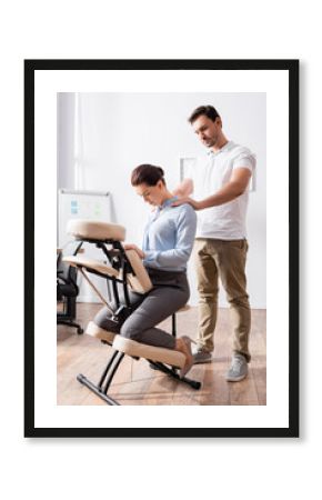 Massage therapist doing seated massage of shoulders for businesswoman sitting in office