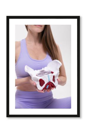 Woman in Lavender Fitness Wear Holding Anatomical Pelvis Model on White Background