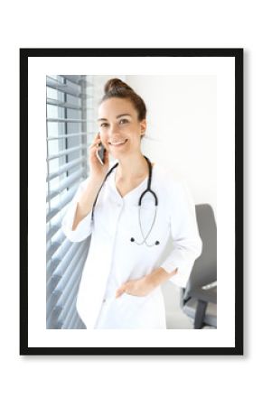 Rozmowa telefoniczna z lekarzem. Lekarka ubrana w biały kitel rozmawia przez telefon stojąc przy oknie.