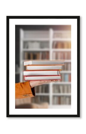 Student hands hold a stack of books in library background.
