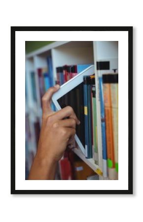 Hand of student keeping digital tablet in bookshelf in library