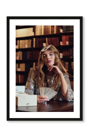 Young beautiful fashionable model sits in a library and plays cards