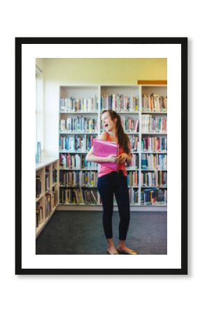 Portrait of happy high school teenage girl holding book binder in library