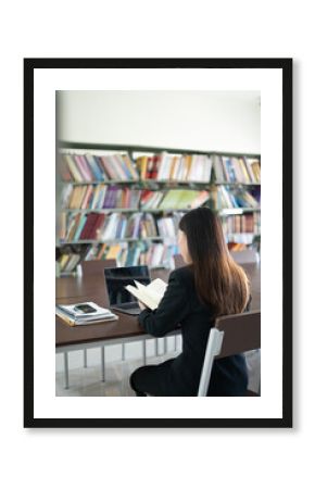 Asian students sit at tables in the library reading, studying, writing, and researching information.
