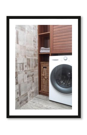 Scandinavian Interiors of laundry room. Wicker laundry basket and clean cotton towels in a wooden closet near a Modern washing machine in a laundry room.
