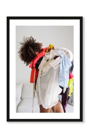 Black woman with afro hair holding pile of clothing standing in the living room