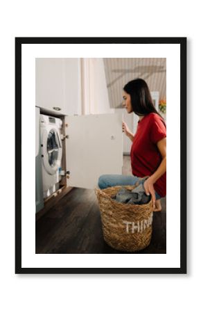 Young woman putting clothes at washing machine while doing laundry