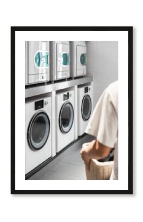 Back view of Asian young man holding laundry basket is preparing to wash clothes in public laundry room.