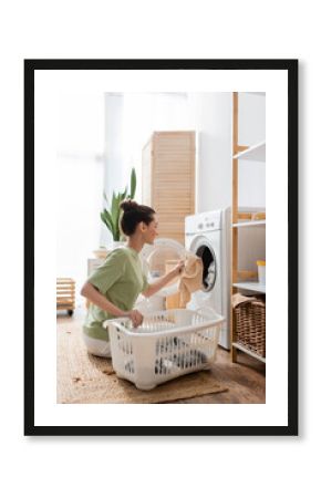 Side view of smiling woman putting clothes in washing machine at home.