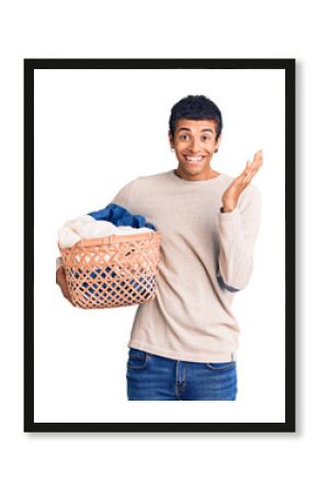 Young african amercian man holding laundry basket celebrating victory with happy smile and winner expression with raised hands