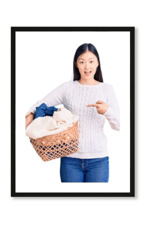 Young beautiful chinese woman holding laundry basket with clothes smiling happy pointing with hand and finger