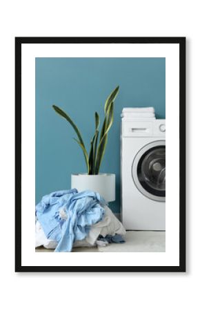 Washing machine, houseplant and pile of dirty laundry near blue wall