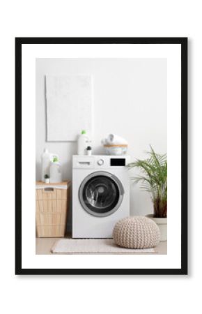 Washing machine with bottles of detergent, laundry basket and pouf near white wall