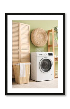 Modern washing machine with basket, shelving unit and dressing screen near green wall. Interior of home laundry room