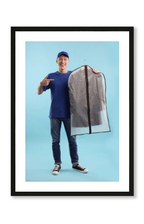 Dry-cleaning delivery. Happy courier holding garment cover with clothes on light blue background