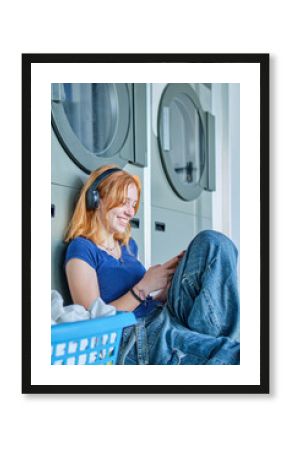 Smiling redhead girl listening to music in a public laundry waiting for her clothes to be washed