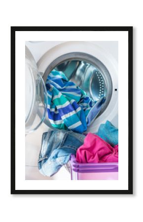 Blue and purple cotton clothes and linen in laundry basket and inside an open washing machine. Vertical.
