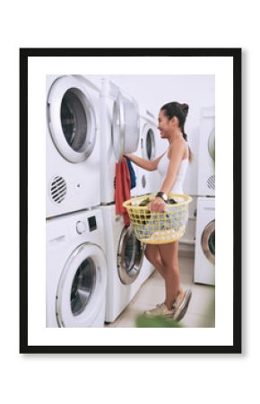 Cheerful young Asian woman loading washing machine in laundry room