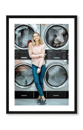 Portrait of a young woman standing near the dryer machines waiting for clothes to be dried in the self serviced laundry