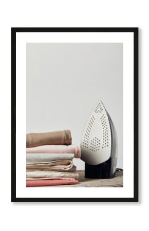 Iron and folded ironed clothes on ironing board isolated on grey