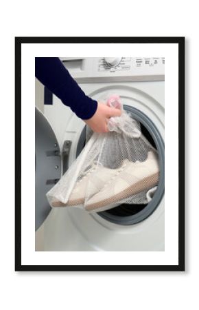 A women holds sports shoes in a laundry bag. Against the background of a washing machine with an open drum.