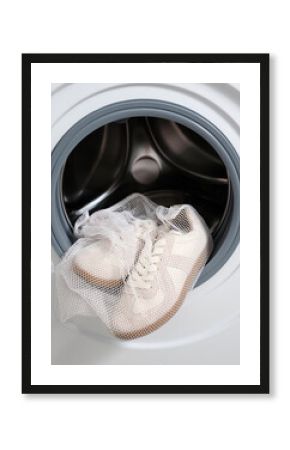 Vertical image of sports shoes in a laundry bag in a washing machine with the drum open.