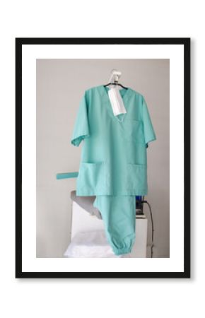 Green medical uniform and mask hanging on an hanger in a laundry.