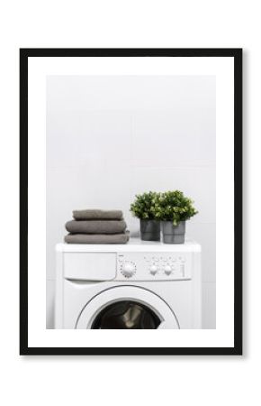 Stacked grey towels and plants in pot on washing machine