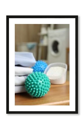 Dryer balls near stacked clean clothes and detergent on wooden table in laundry room