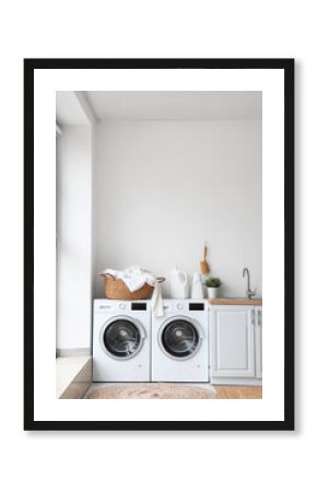 Basket with dirty clothes and detergent on washing machines in laundry room