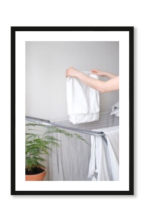 Woman or housewife taking clean clothes from drying rack at home