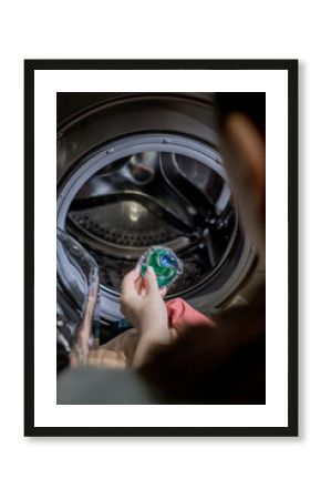 Woman putting laundry detergent capsule into washing machine indoors, closeup. Washing clothes.The concept of washing and cleanliness