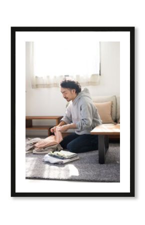 Asian (Japanese) man doing housework folding laundry in the living room.