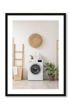 Modern washing machine with basket, houseplant and ladder near white wall. Interior of home laundry room