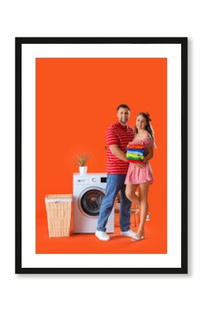 Happy young couple with laundry near washing machine on orange background