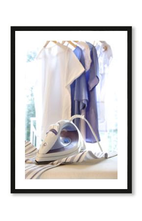 Iron on ironing board with clothes hanging