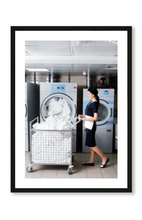 happy maid looking at dirty bedding while standing near metallic cart