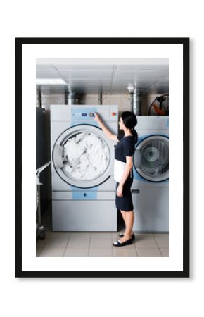 brunette maid standing and touching button on washing machine in laundry