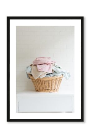 Vertical view of pink towel and blue sheets in wicker laundry basket on white table against painted brick wall (selective focus)