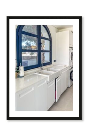 Modern laundry room featuring a spacious white countertop, large sink, and washing machine, illuminated by natural light through a blue-framed window, showcasing a clean and organized space