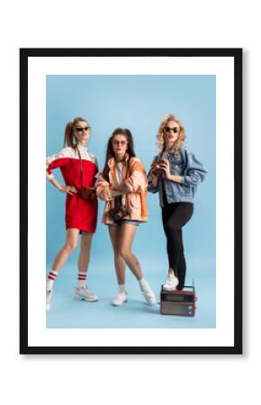 Pretty young women in retro 90s fashion style, outfits posing isolated over blue studio background. Concept of eras comparison, beauty, fashion and youth.