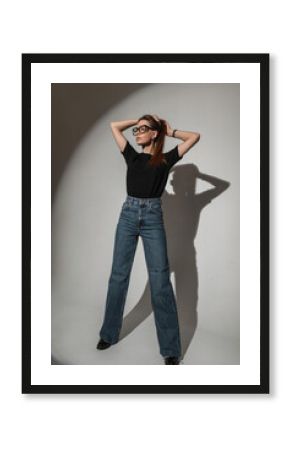 Stylish beautiful glamorous young woman with vintage glasses in a black t-shirt with blue fashion jeans in the studio
